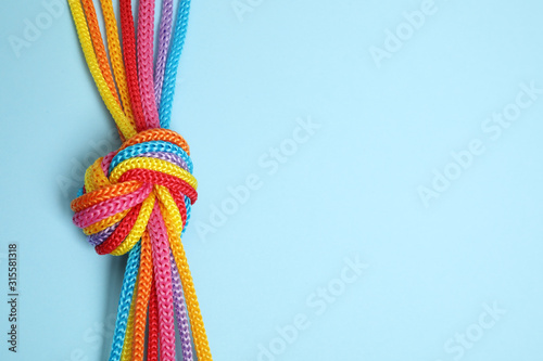 Top view of colorful ropes tied together on light blue background, space for text. Unity concept