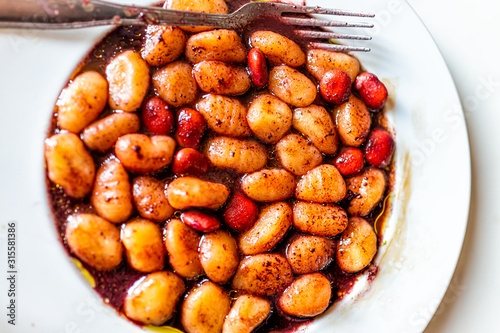 Closeup flat top view above of vibrant red wine sauce potato gluten free wheat gnocchi on white plate with lupine beans marinated in Italian Italy restaurant olive oil
