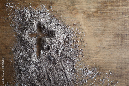 Christian cross symbol made of ash on a wooden background