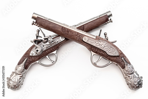 Firearms dating to the american revolution and antique collectables concept with ornate old fashioned dueling flintlock pistols crossed in duel isolated on white background with clipping path cutout