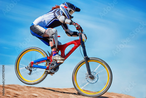 Downhill. Speed race. Woman on a red bike against the blue sky. Extreme sport.