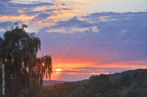 Untergehende Sonne in Abenddämmerung vor einem grünen Wald- und Hügelpanorame in prächtigen Farben in Deutschland