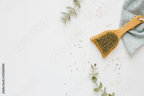  White spa background with eucalyptus, body brush, salt and a towel, flat, top view