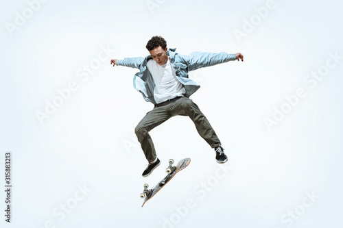 Caucasian young skateboarder riding isolated on a white studio background. Man in casual clothing training, jumping, practicing in motion. Concept of hobby, healthy lifestyle, youth, action, movement.