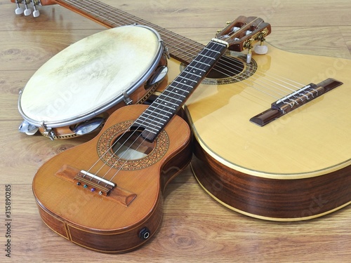 An acoustic guitar and two Brazilian musical instruments: cavaquinho and pandeiro (tambourine), on a wooden surface. The instruments are widely used to accompany samba and choro music.