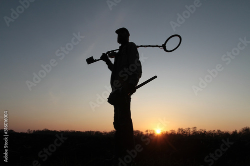 Silhouette of a man with a mine detector on the background of the setting sun