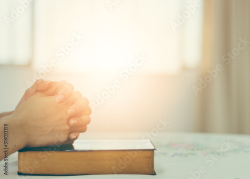 The hand of a Christian woman rests on the Bible to pray for God.