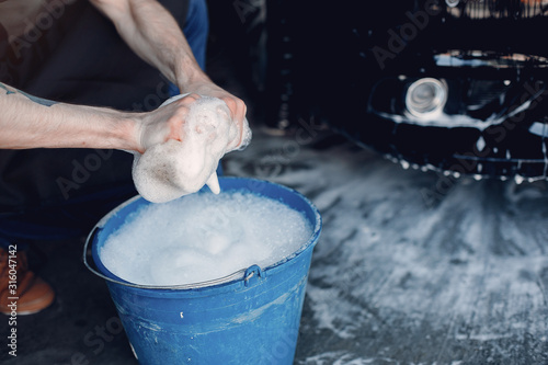 Man in a garage. Worker washing a car. Guy with a bucket ans sponge