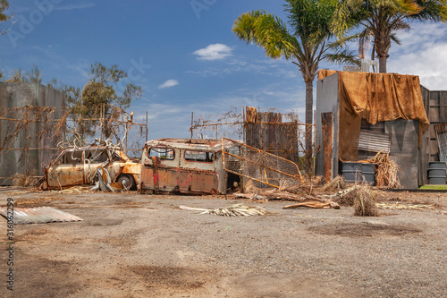 rusty car and truck next to a metal fence in a junkyard