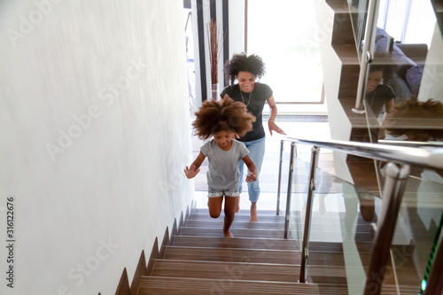 Excited African American mom and daughter run upstairs new home