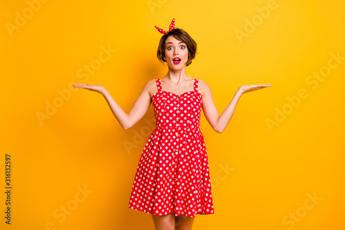 Photo of pretty lady model manager hold open arms product presenting cool novelty two variants wear retro style summer dotted red white dress headband isolated yellow color background