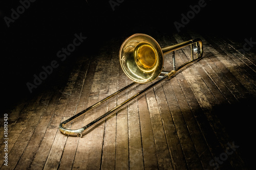 golden brass instrument trombone lies on a dark brown wooden stage in the rays of light.