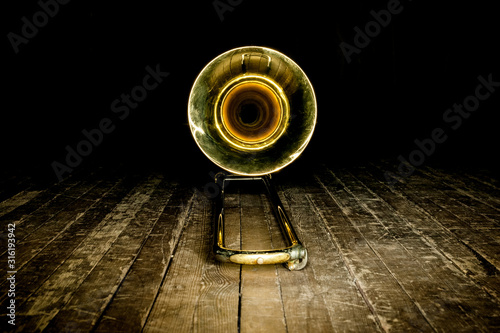 yellow brass instrument trombone lies on the wooden floor of the stage. front view on the bell