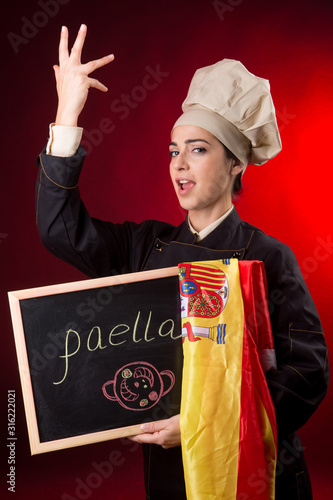 cuoca spagnola con bandiera e lavagna con su scritto paella