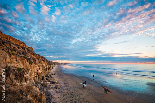 Elevated perspective of a beach at sunset with surfers and puffy clouds