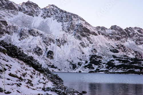 Jezioro górskie. Tatry Wysokie. Dolina Pięciu Stawów. Czarny Staw. Szczyty gór pokryte śniegiem. 