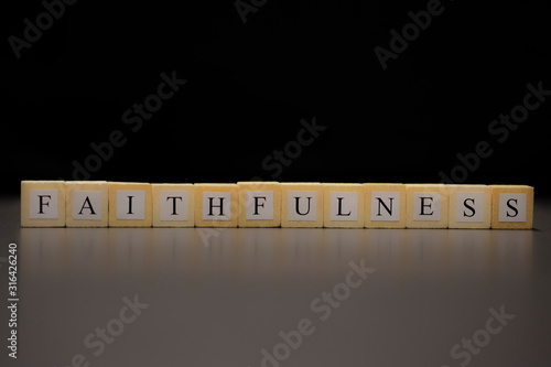 The word FAITHFULNESS written on wooden cubes isolated on a black background..