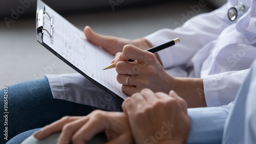 Close up doctor filling older patient checkup form, documents