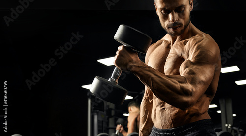 Male bodybuilder training biceps with dumbbell.
