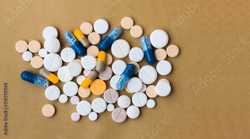 Heap of colorful pills, pharmaceutical medicine tablets and capsules on beige yellow background. Drug prescription for treatment medication health care concept, top view with copy space.