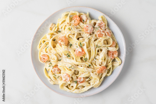 Italian pasta fettuccine or tagliatelle in a creamy sauce with shrimps in a plate on white marble table