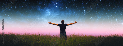 Man with arms wide open standing on the grass field against the night starry sky. Elements of this image furnished by NASA.