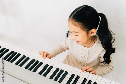 From above of happy smiling cute Asian girl playing piano enjoying time practicing music at home