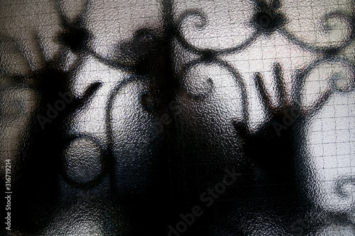 Figure of mysterious stranger pressing hands against a textured glass door with security bars