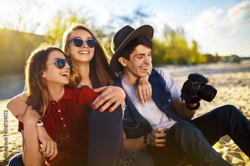 Group of happy friends spending time together at the beach. Young friends are having fun at sunset on the beach. Group of smiling people in sunglasses enjoy photos. Summer, holidays, vacation concept 