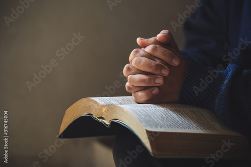 Hands folded in prayer on a Holy Bible in church concept for faith