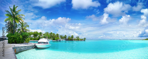 White Boat at pier with palm trees, Maldives island. Beautiful panoramic tropical landscape with turquoise ocean and blue sky with clouds.