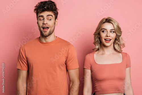 positive, tricky man and woman looking at each other on pink background