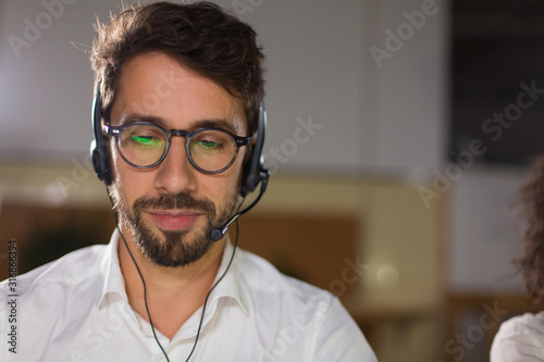 Front view of call center operator with headset. Confident young man in eyeglasses looking at screen. Call center concept