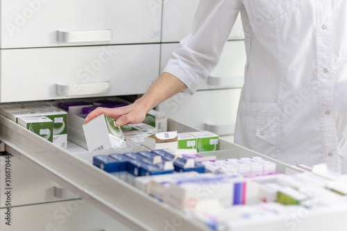 Pharmacist holding medicine box and capsule pack in pharmacy drugstore.