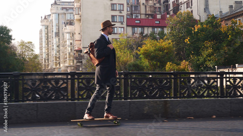 Hipster businessman skateboarding at the bridge at sunny day
