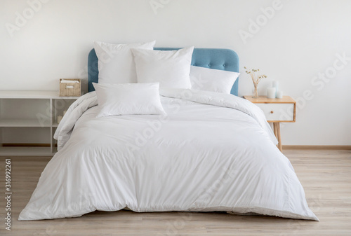 Interior with white bed linen on the sofa. Bedroom with bed, white bedding, and bedside table. White pillows, duvet and duvet case on bed with blue headboard. Front view.