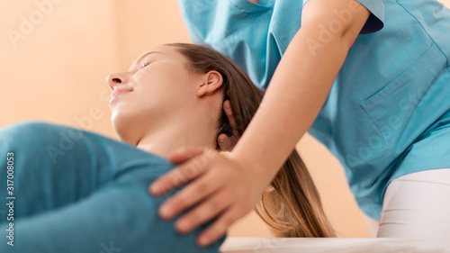 Female physiotherapist or a chiropractor adjusting patients neck. Physiotherapy, rehabilitation concept. Side view cropped shot.