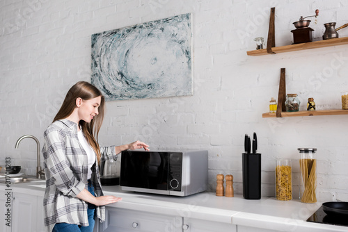 side view of smiling woman looking at microwave in kitchen