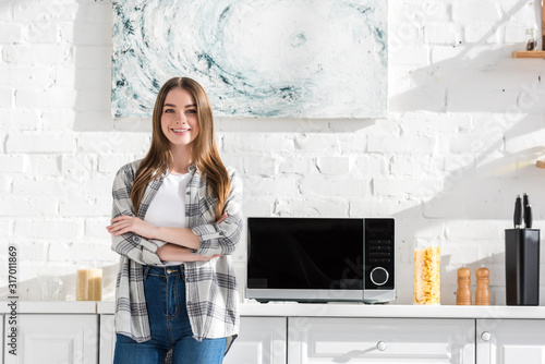 smiling and attractive woman standing near microwave in kitchen