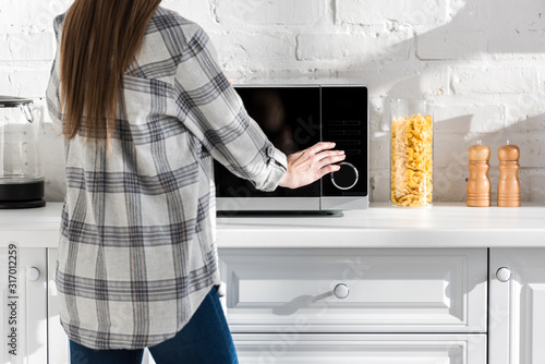 cropped view of woman in shirt using microwave in kitchen