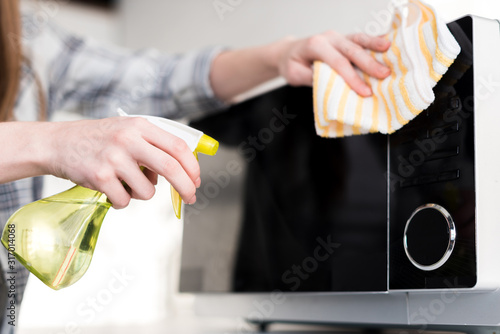 cropped view of woman cleaning microwave with rag in kitchen