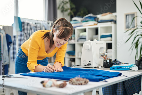 Charming caucasian smiling dedicated seamstress drawing seam with chalk on a skirt.