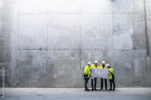 A group of engineers standing against concrete wall on construction site.