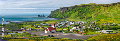 Panoramic view of basalt stacks Reynisdrangar, black sand beach, church and city of Vik at South Iceland, summer time