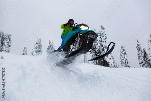 Adventurous Man Riding a Snowmobile in white snow. Taken near Squamish and Whistler, British Columbia, Canada.