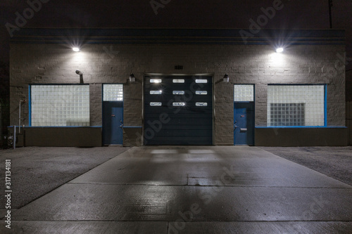 Two blue doors and a large garage door on the back of an industrial building at night with star burst lights