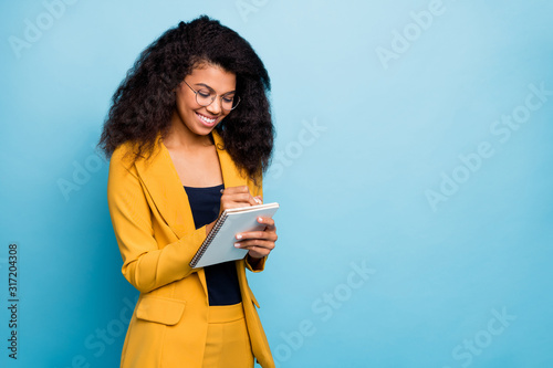 Photo of beautiful dark skin business lady creative writer noting nice thoughts on paper planner writing to-do list wear specs stylish yellow office suit isolated blue color background