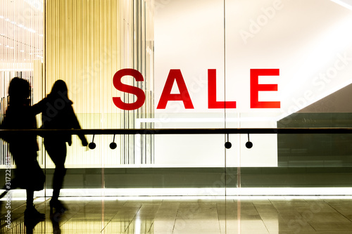 Silhouetted shoppers walking past shop window sale sign