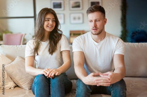 young couple man and woman sitting on the sofa both looking embarrassed , grimacing mood