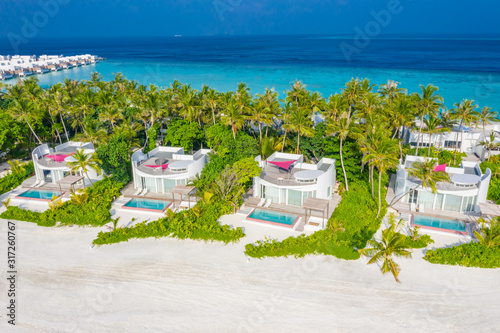 Maldives coastline, aerial landscape of luxury villas with white sand and palm trees. Paradise island aerial view, amazing blue sea and luxury vacation background